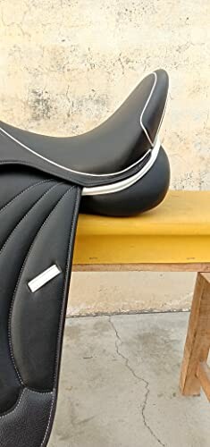 Black leather horse saddle on a wooden bench.